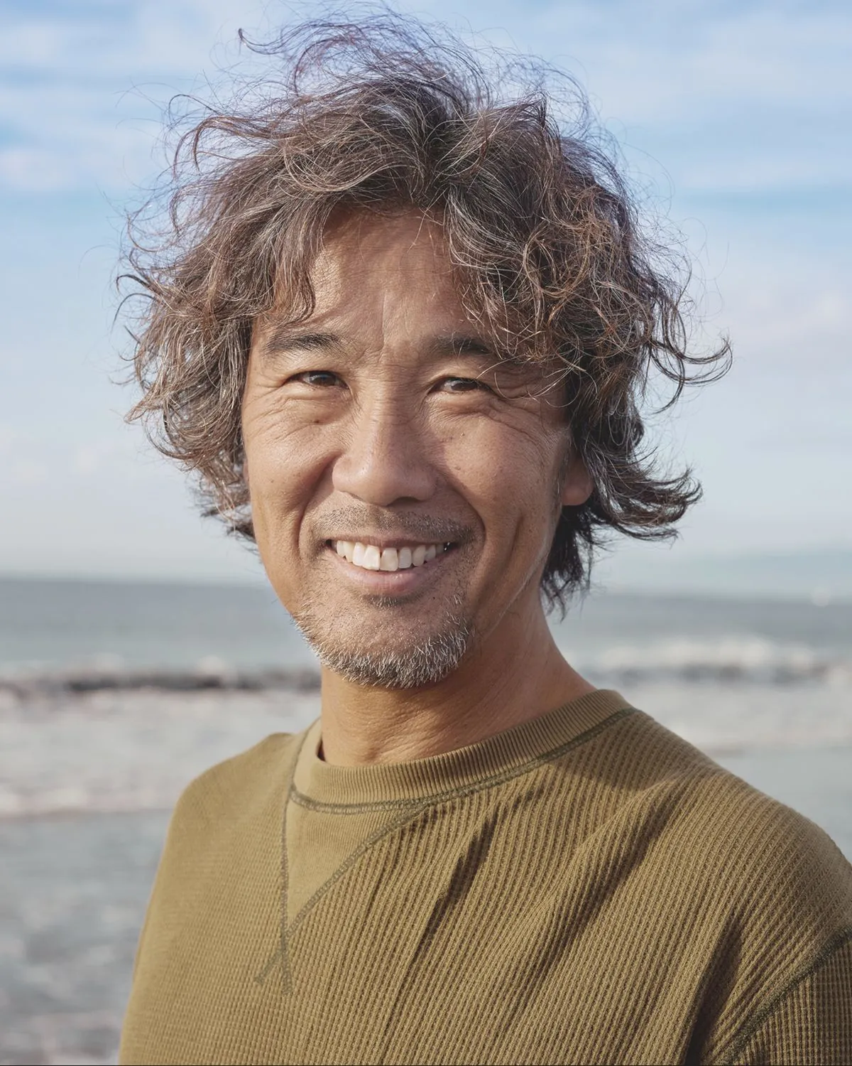 A smiling man with curly hair on a beach