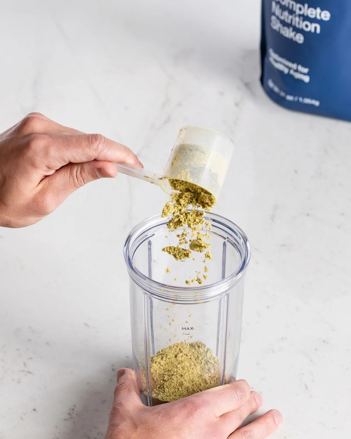 A scoop of powder being added to a blender cup